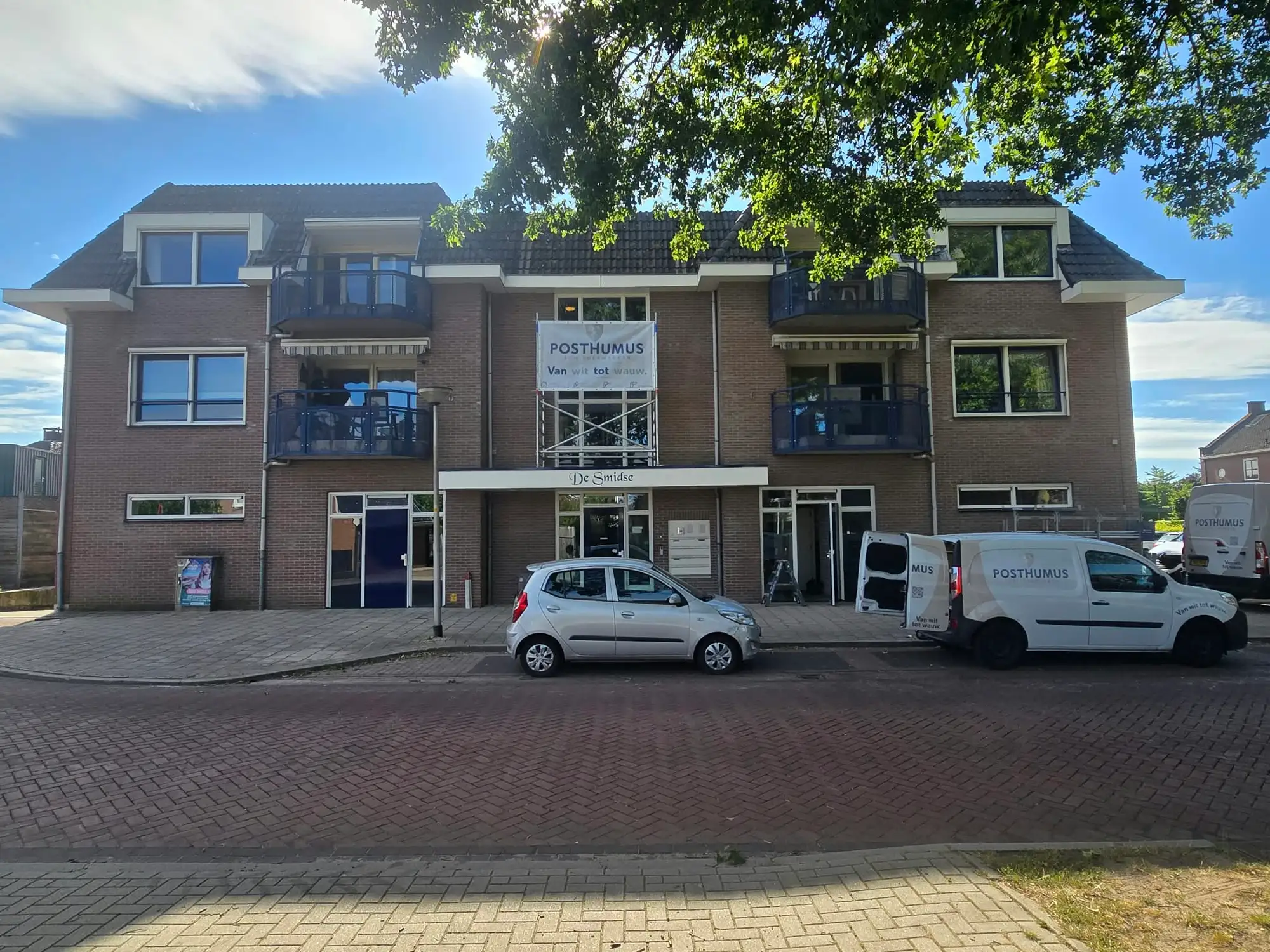 Twee bestelbussen van Posthumus Schilderwerken voor appartementencomplex De Smidse in Wierden, met een banner van het bedrijf aan de steiger tijdens het VvE-schilderwerk