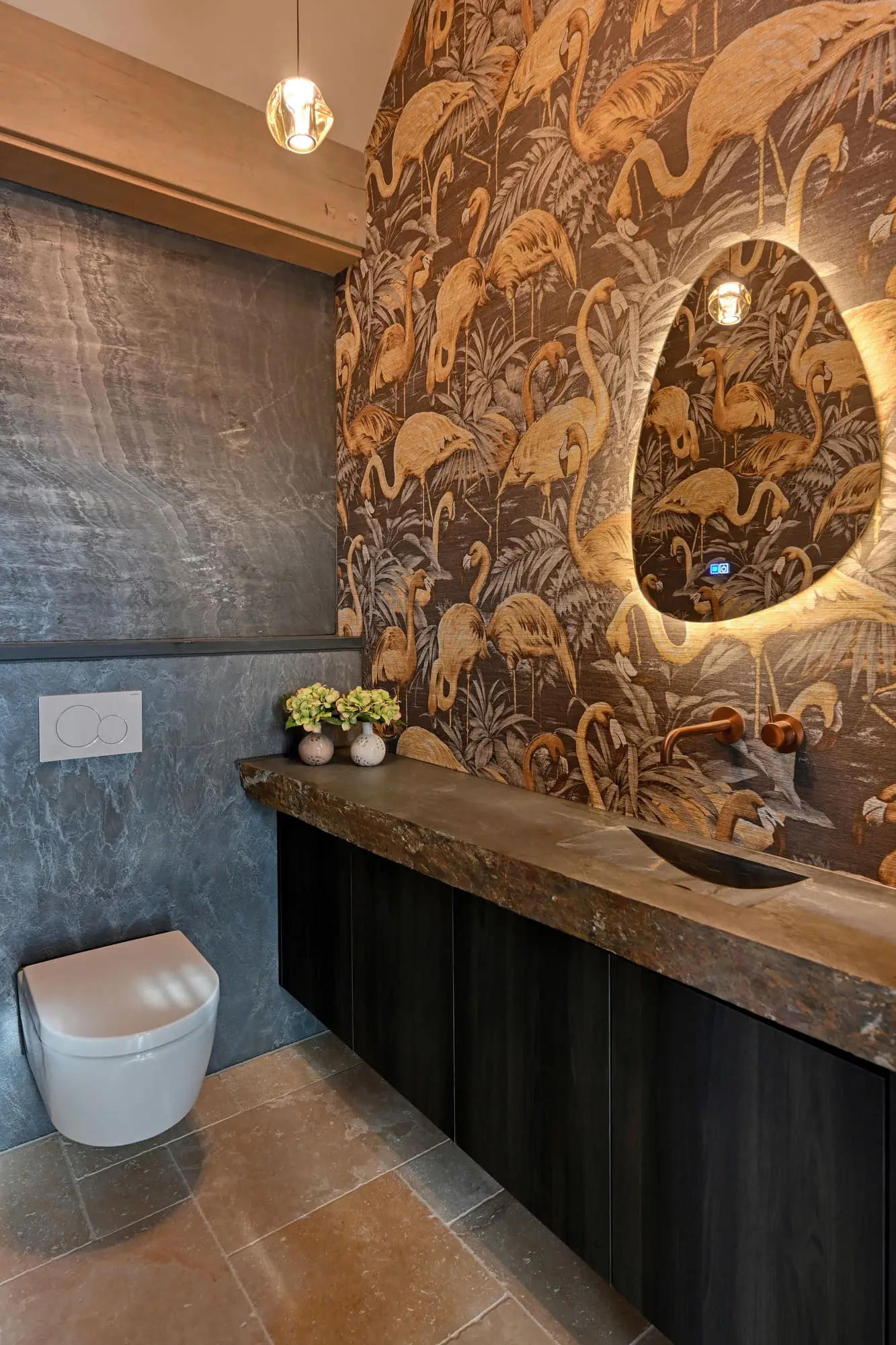 Toiletruimte met een wand vol donker behang met een flamingopatroon, een natuurstenen wastafelblad en een verlichte spiegel