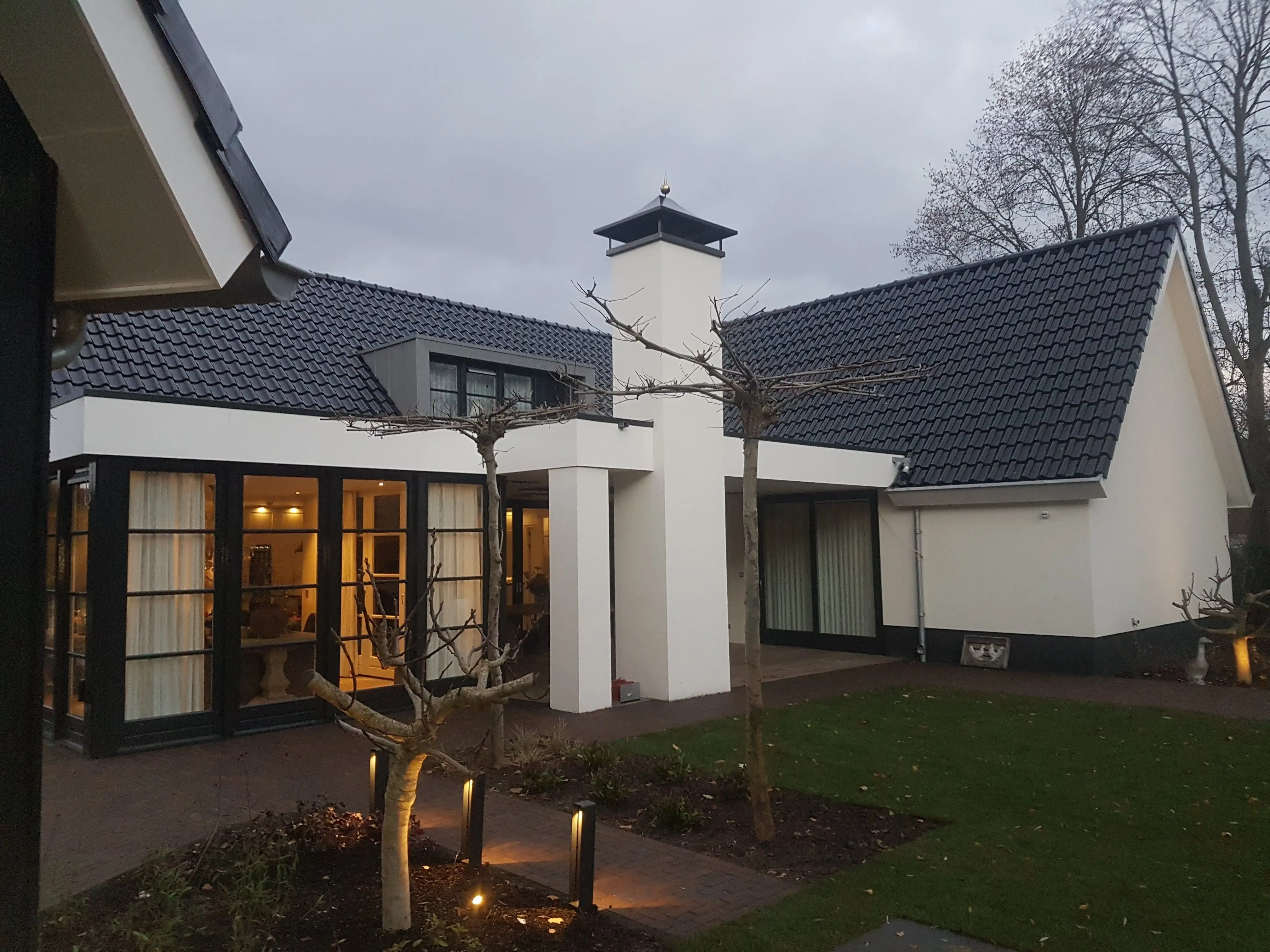 Wit gestuukte villa in de schemering met antracietgrijze kozijnen en dakgoten, na buitenschilderwerk