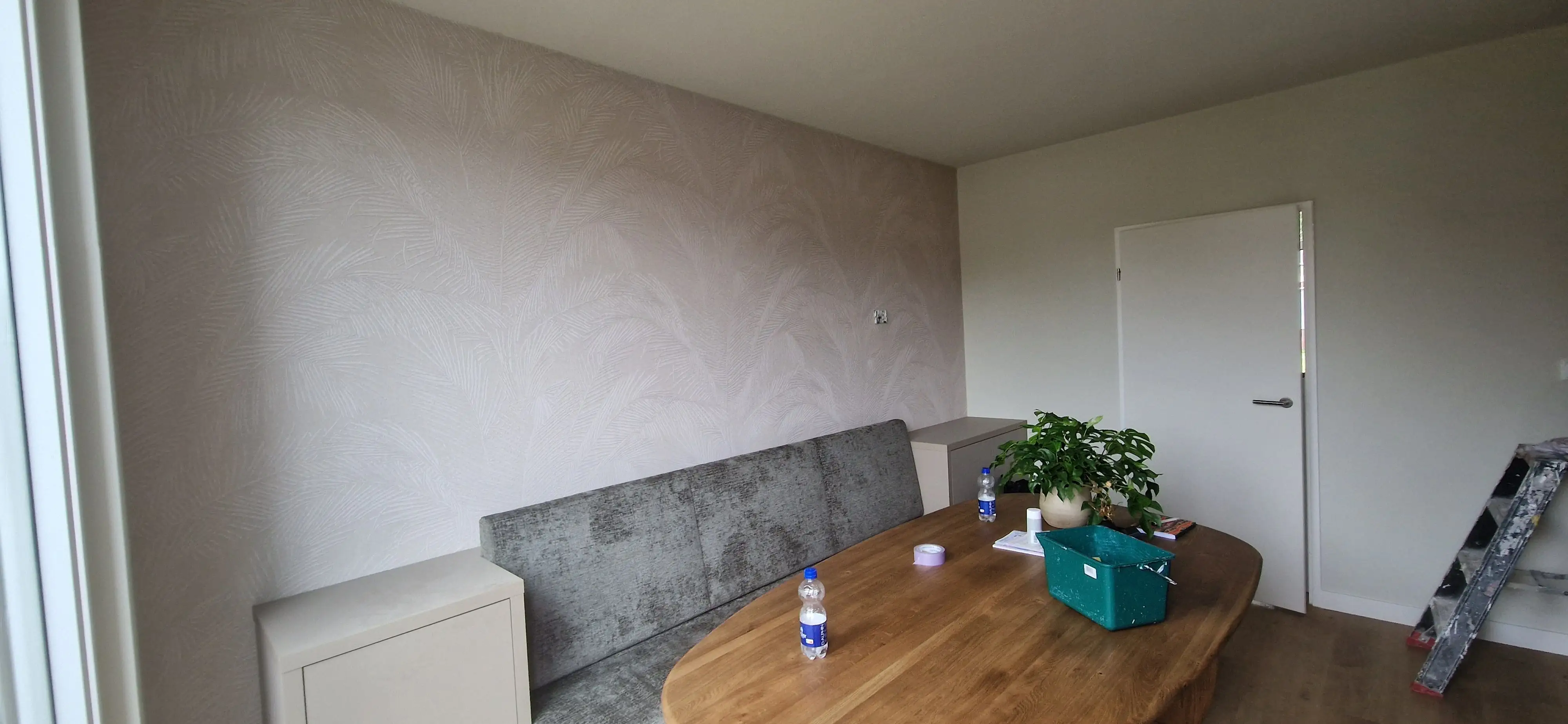 Eethoek met een wand vol vliesbehang met een licht bladpatroon, na het behangen