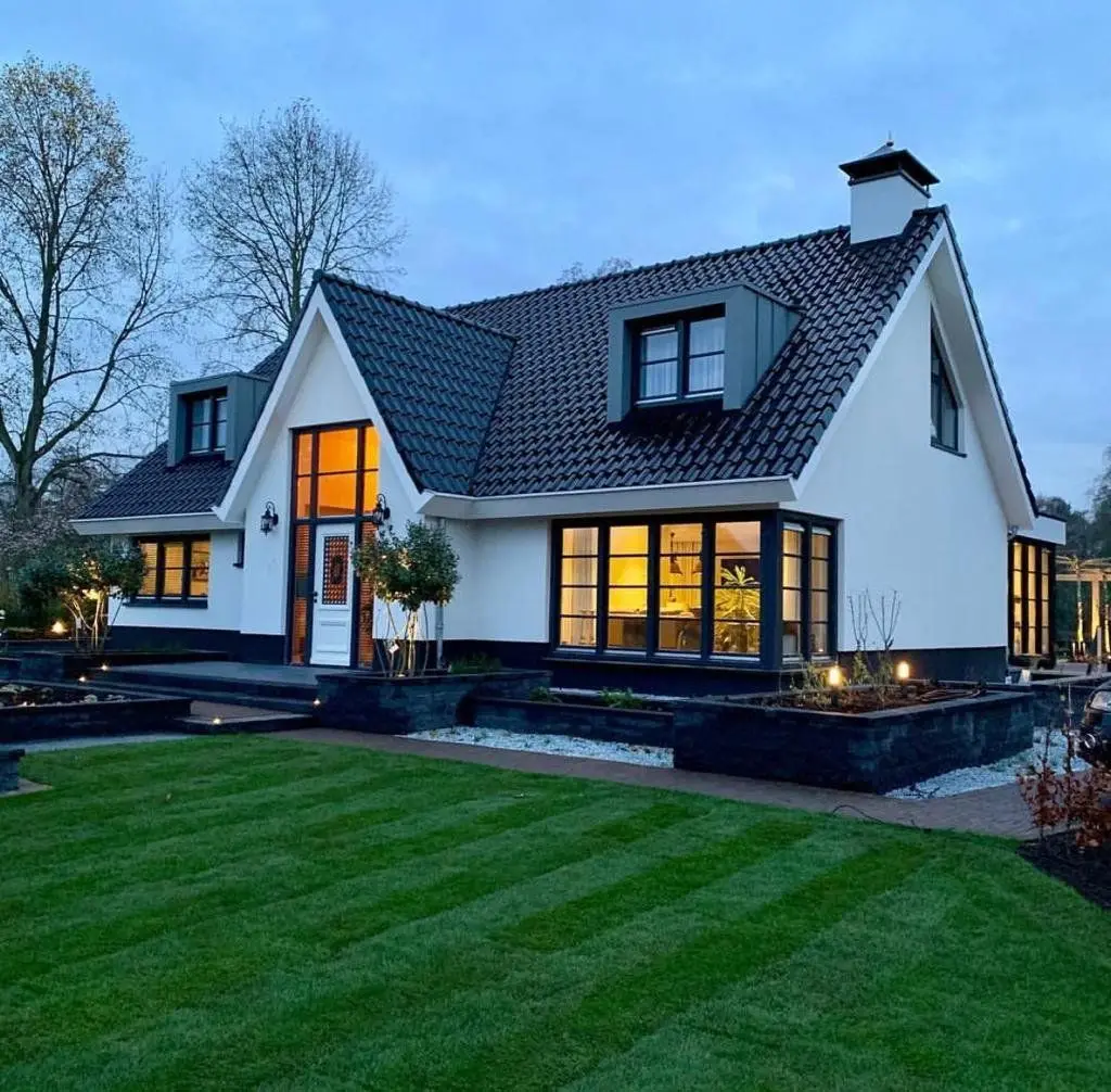 Woonhuis in de avond met verlichte ramen, houten kozijnen en luiken